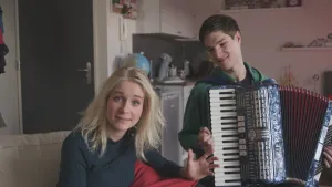 Foto van presentator bij een jongeman, jongen, die op een accordeon speelt.