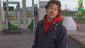 Foto van presentator die staat bij een pompstation, tankstation, voor auto's.