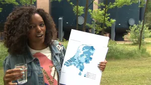 Foto van presentator die een kaart van Nederland in haar hand houdt die aangeeft het kalkgehalte in het water per gebied.
