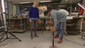 Foto van man en vrouw in een werkplaats, de man doet iets met een fietspomp.