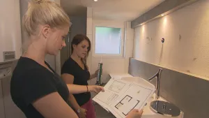 Foto van twee vrouwen die in een WC-ruimte staan, één van hen houdt een soort plattegrond vast.