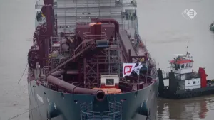 Foto van een grote boot op het water met op het dek één of andere grote machine van diepzeemijnbouw met buizen etc., ernaast ligt een klein bootje.