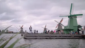 Foto van water met eromheen vele molens waar mensen lopen, ook staat daar presentator, de Zaanstreek.