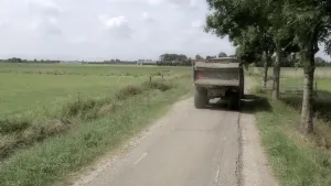 Foto van weggetje langs groot weiland waarover een landbouwvrachtautootje rijdt.