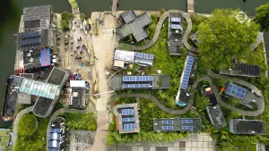 Foto van een woonwijk aan het water met veel zonnecellen op de daken, recht van bovenaf genomen.