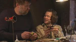 Foto van Harry die Kosmotroniks, soort minivoertuigjes, maakt aan tafel, erbij zit presentator.