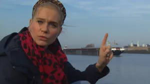 Foto van presentator die staat bij groot kanaal waarop een vrachtboot vaart.