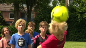Foto van een groep jongens buiten aan het voetballen, eentje van hen maakt een kopbal.
