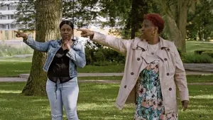 Foto van twee donkere vrouwen die staan in een park bij de Bijlmer flat, ze wijzen beiden ergens naartoe.