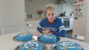 Foto van presentator die aan tafel zit waarop aantal blauwe taarten met het Euro-symbool erop staan.