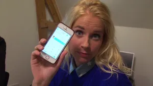 Foto van vrouw, je ziet haar gezicht en haar hand die een mobiele telefoon, smartphone, vasthoudt met op het beeldschermpje iets van een tabel.