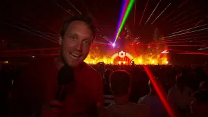 Foto van presentator die staat in grote zaal waar een festival aan de gang is met veel laserlicht, laserstralen.