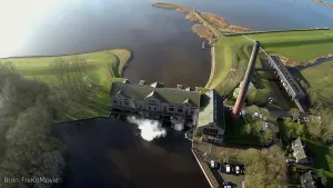 Foto van deel van het IJsselmeer, je ziet deel van het land waarop een ouderwetse fabriek staat.