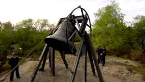 Foto van de klok op de Waalsdorpervlakte die geluid wordt door aantal mannen.