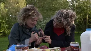 Twee vrouwen die aan tafel zitten, de ene geeft de andere een insulineprikje in de vinger.