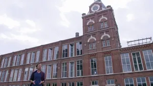 Foto van een oud industrieel gebouw, monumentaal, op de voorgrond staat presentator.