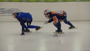 Twee jongens met helmpjes op die schaatsen, shorttrack, op een indoor ijsbaan.