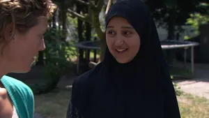 Foto van gesluierde vrouw in gesprek met presentator, buiten in een tuin met mooi weer.