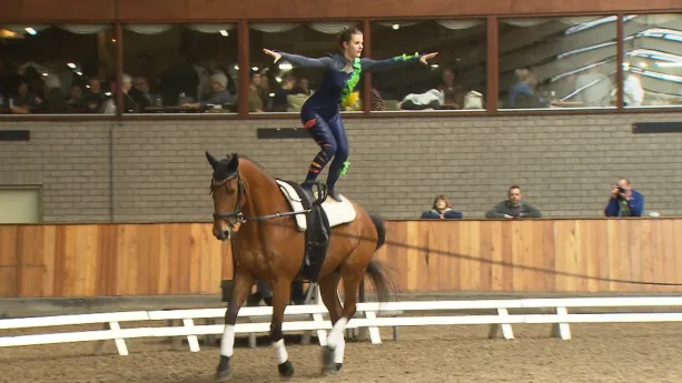 Foto van een turnster die staat op een lopend paard in manege.