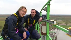 Foto van twee mannen in werkkleding die staan op de top van een hoge achtbaan, foto van dichtbij genomen.