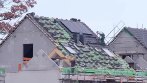 Foto van twee werkmannen die bezig zijn aan het dak van een modern huis met ook zonnecellen erop.