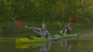 Foto van twee kano's, eenpersoons, in de ene zit een vrouw, in de andere een man, ze varen op een vaart in de natuur, de Biesbosch.
