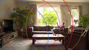 Foto van vrouw die op de bank zit in een huiskamer, over de foto zijn allerlei grote cirkels van verschillende kleuren getekend.