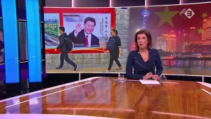 Foto van presentator aan tafel in de studio, op achtergrond grote foto van de Chinese President.
