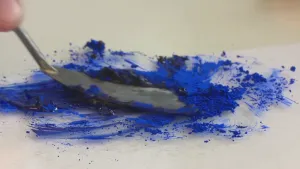 Foto, van dichtbij genomen, van een soort kleine spatel die een blauwe poedervormige kleurstof bewerkt.