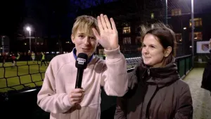 Foto van jongen met microfoon, naast hem staat een meisje, buiten op straat, het is donker.