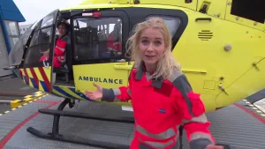 Foto van presentator in werkkleding die staat voor een gele traumahelikopter.