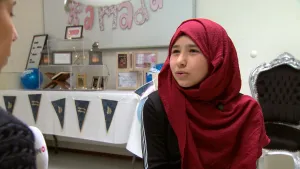 Foto van meisje met hoofddoek in een ruimte met feestelijk gedekte tafel met erboven slinger met de tekst "Ramadan".