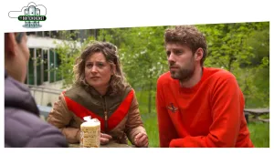 Foto van twee mannen en een vrouw die zitten aan tafel in een tuin, op tafel staat een rol koeken/crackers.