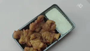 Foto van een bakje met gebakken kibbeling, vis, met saus erin.