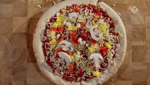 Foto van een handgevormde pizza, met o.a. champignons en paprika erop, van bovenaf gezien.