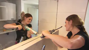 Foto van vrouw die in badkamer bezig is bij de spiegel met een lijmspuit, je ziet haar ook terug in die spiegel.