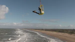 Iemand die van het platformpje af springt van bungeejumpen, boven de zee aan het strand.