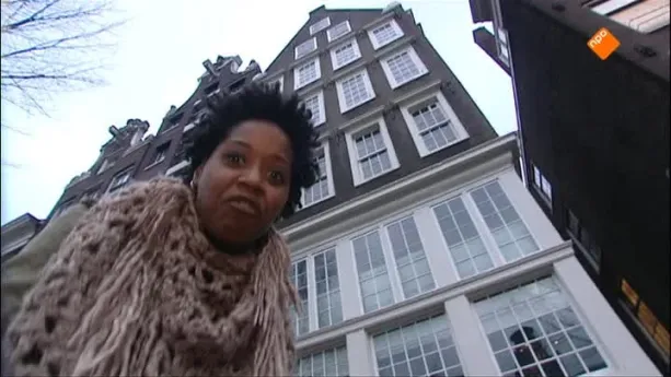 Foto van presentator die staat voor aantal hoge Amsterdamse grachtenpanden.