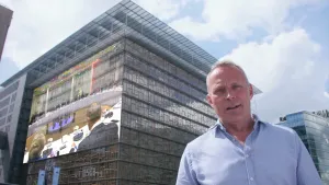 Foto van presentator die staat voor een groot modern gebouw, van de Europese Unie.