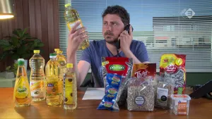 Foto van presentator die aan tafel zit met daarop aantal flessen zonnebloemolie en andere producten zoals zonnebloempitten.