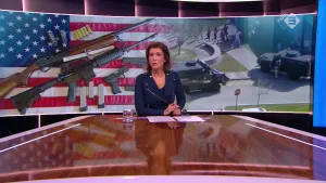 Foto van nieuwslezeres die aan de desk zit met op de achtergrond grote foto van de Amerikaanse vlag met allerlei geweren/wapens erop.