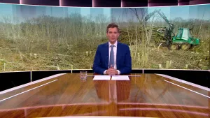 Foto van presentator die aan de desk zit met op de achtergrond grote foto van een gekapt bos waarbij een graafmachine aan het werk is.