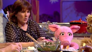 Foto van Sesamstraat waarbij vrouw aan tafel zit met Purk, op tafel staat glazen schaal met eten erin.