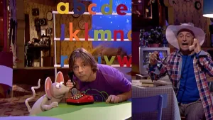 Foto van Sesamstaat waarbij presentator zit aan tafel met Ieniemienie , man met telefoon, die telefoneert, komt eraan gelopen.