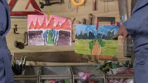 Foto van twee verftekeningen, schilderijen, die aan waslijn hangen te drogen in een atelier.