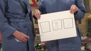 Foto van iemand die een vel papier vasthoudt met daarop drie kleinere tekeningen: een droevig emoticon, hand die bloemen vasthoudt, een vrolijke emoticon.
