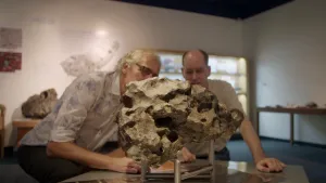 Foto van twee mannen die in een kamer staan bij een grote meteoriet die staat op tafel.