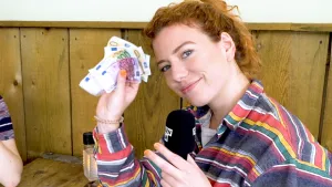 Foto van presentator met microfoon in haar ene hand, in de andere hand een bundel van verschillende Eurobiljetten.