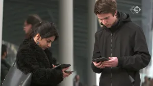 Foto van jongen en meisje die buiten bij gebouw kijken op telefoon, smartphone.