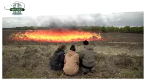 Foto van drie personen die gehurkt zitten op een vlakte, voor hun staat groot deel van die vlakte in brand.